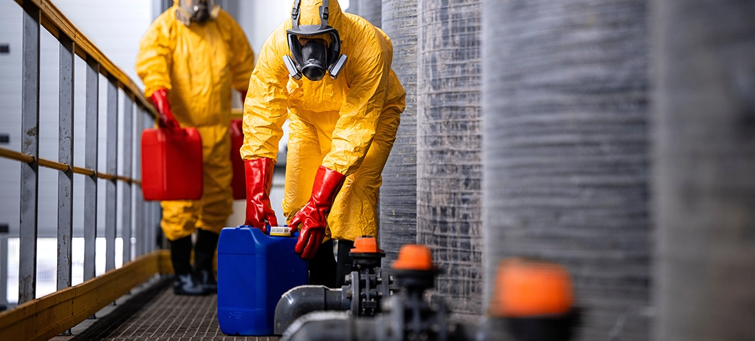 Two people in hazmat suits and respiratory masks working with hazardous chemicals.